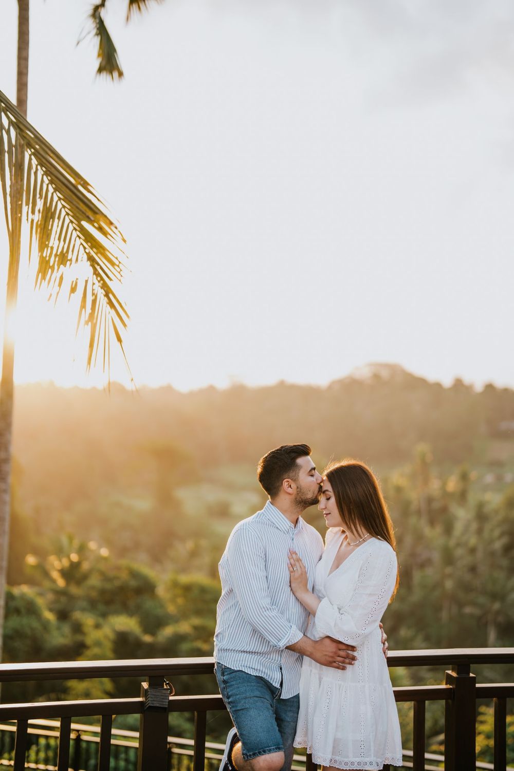 Romantic sunset embrace on balcony overlooking tropical landscape.