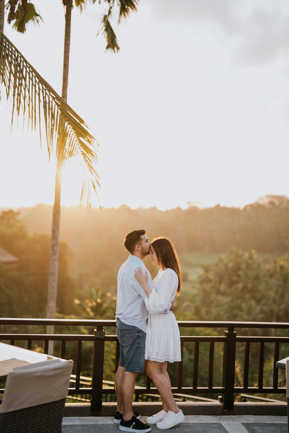 A romantic sunset engagement photo session on a tropical balcony with palm trees in the background.