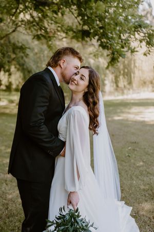 Newlyweds share intimate moment while holding greenery bouquet in outdoor garden setting.  christchurch wedding photography