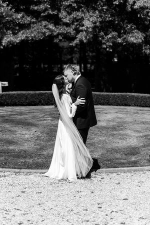 Black and white wedding photograph capturing an intimate moment between newlyweds on a gravel path outdoors. christchurch wedding photo