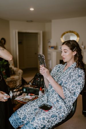 Person wearing blue and white floral robe relaxes in chair while looking at phone. christchurch wedding photography