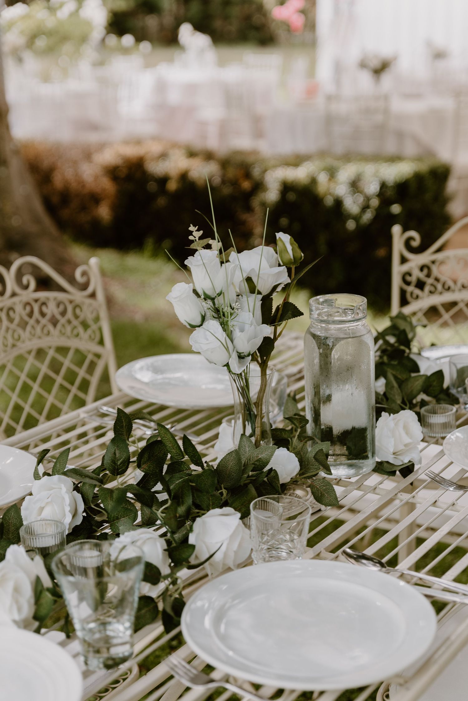 Long white dinner table set outdoors with vintage decor, mason jars, and elegant floral arrangements for a garden wedding. christchurch