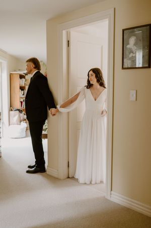 First look moment captured as bride and groom stand on opposite sides of white door. christchurch wedding photography