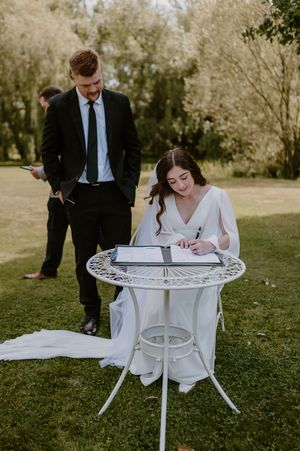 A couple signs marriage documents at an outdoor wedding ceremony using a decorative white table. christchurch wedding photography