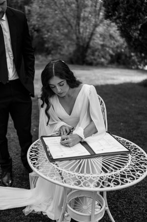 A bride signs documents at a decorative white metal garden table outdoors. christchurch wedding photography