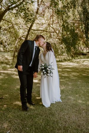 Romantic first look between couple in white dress and black suit outdoors under green trees. christchurch wedding photography