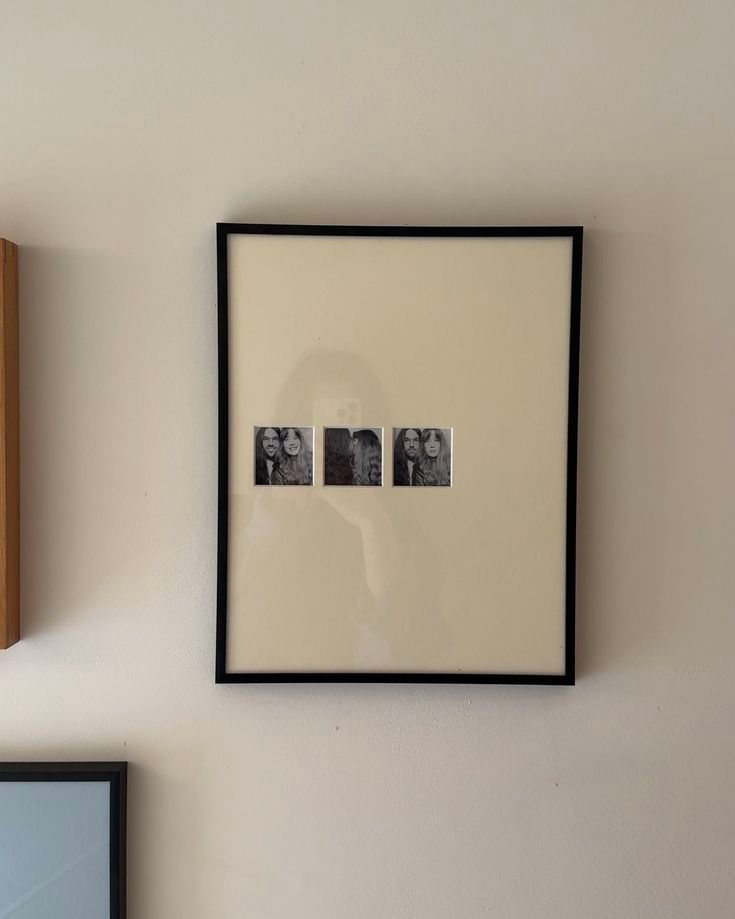 A gallery wall arrangement of minimalist black-framed artwork and photographs against a white painted wall.