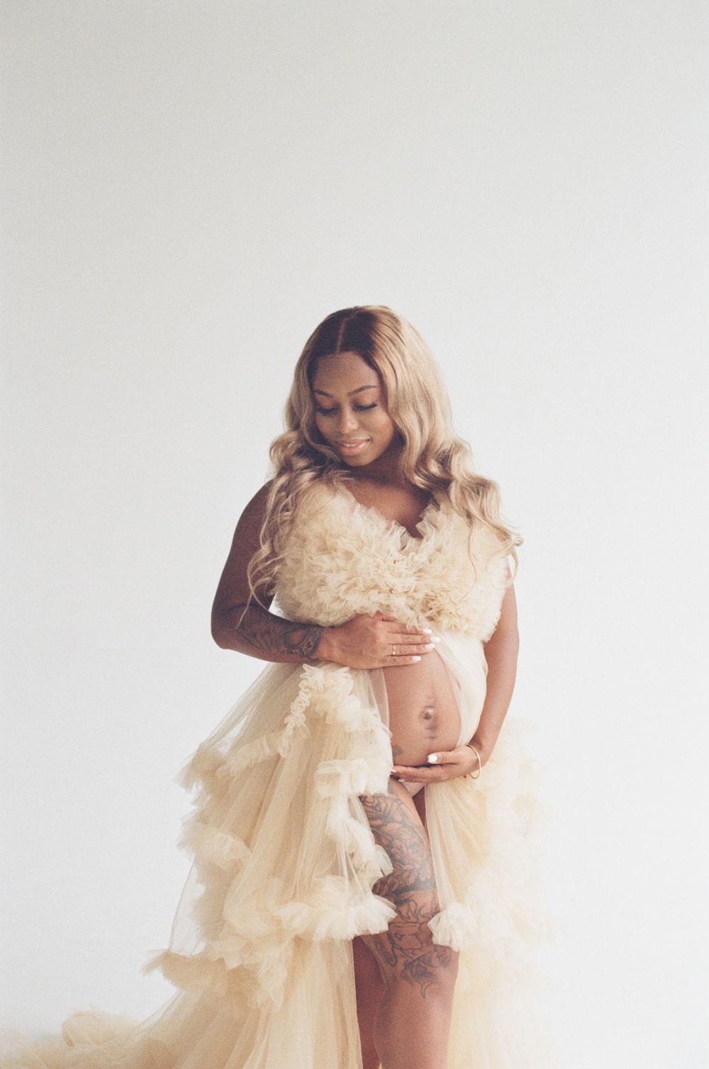 Maternity portrait in flowing cream tulle dress against white backdrop.