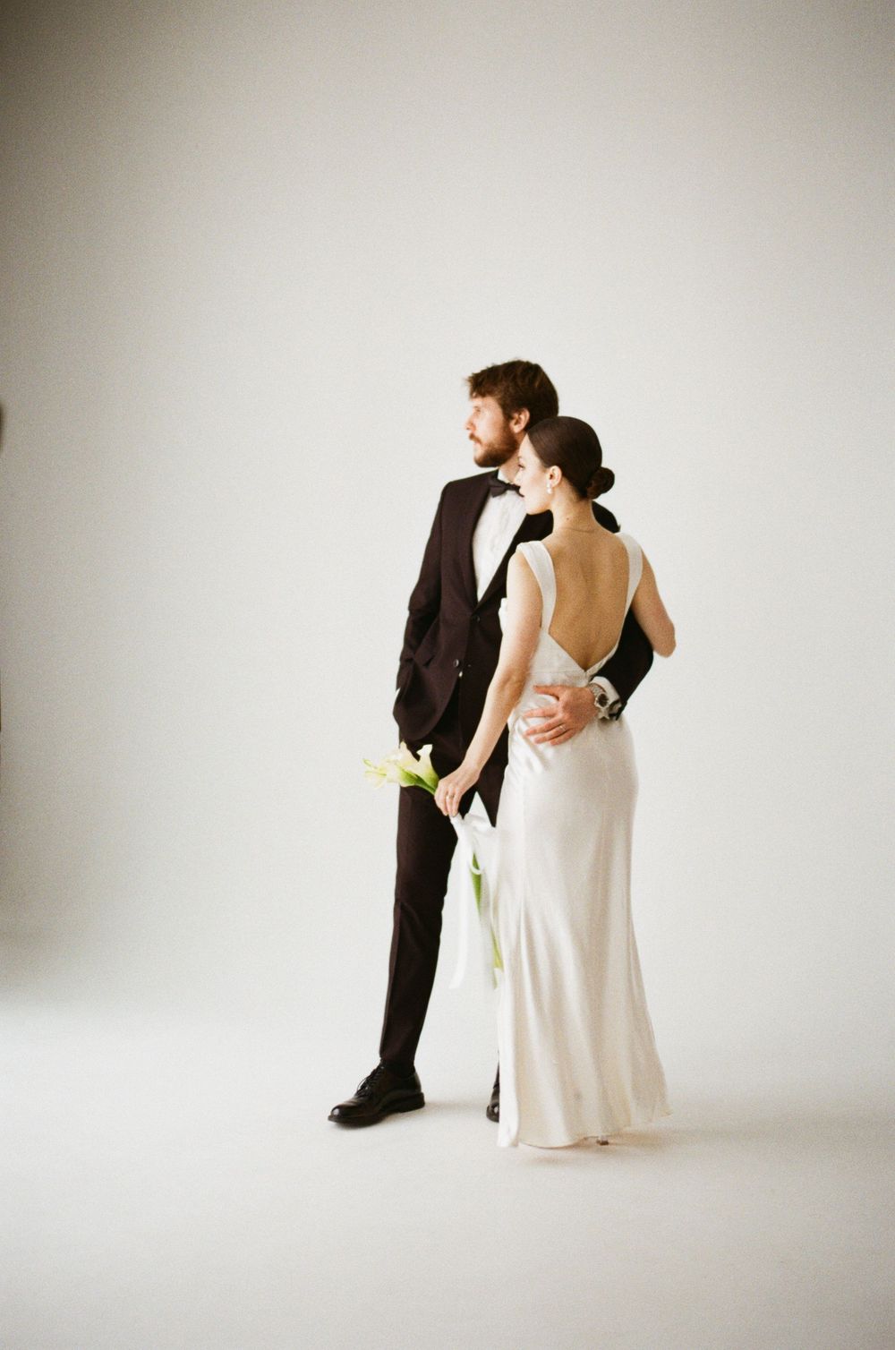 Artistic wedding portrait against white backdrop featuring couple in formal attire with minimal styling.