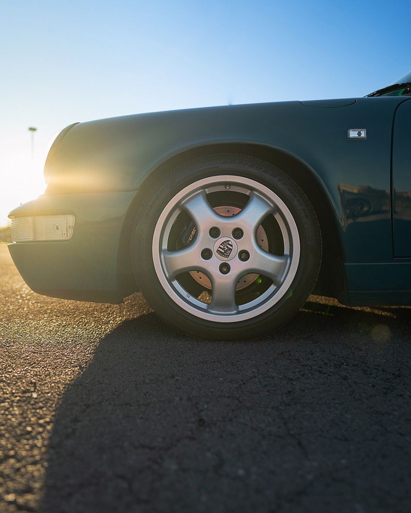 Close-up of sports car wheels and fenders at sunset with dramatic lighting.
