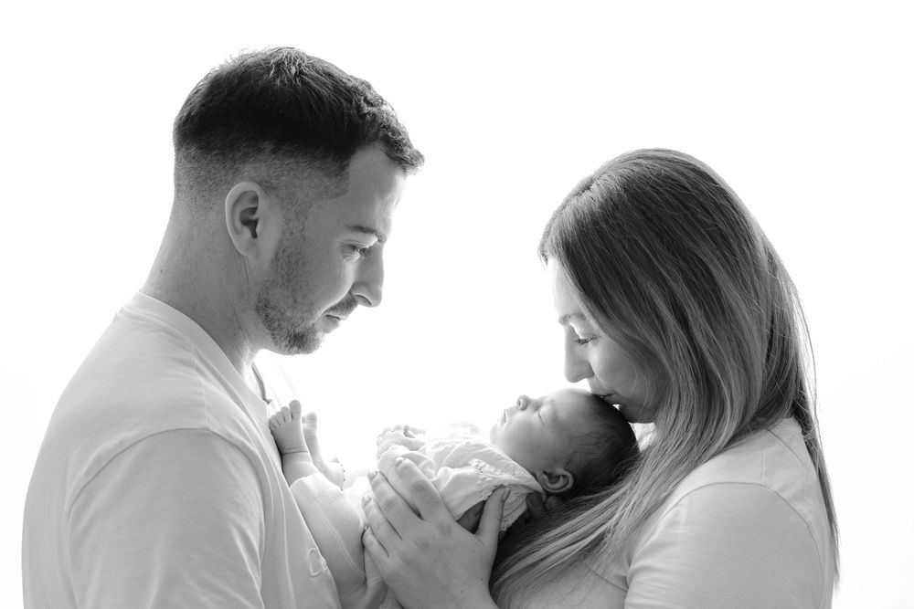 Black and white photo of parents lovingly gazing at their newborn baby in a bright studio setting.