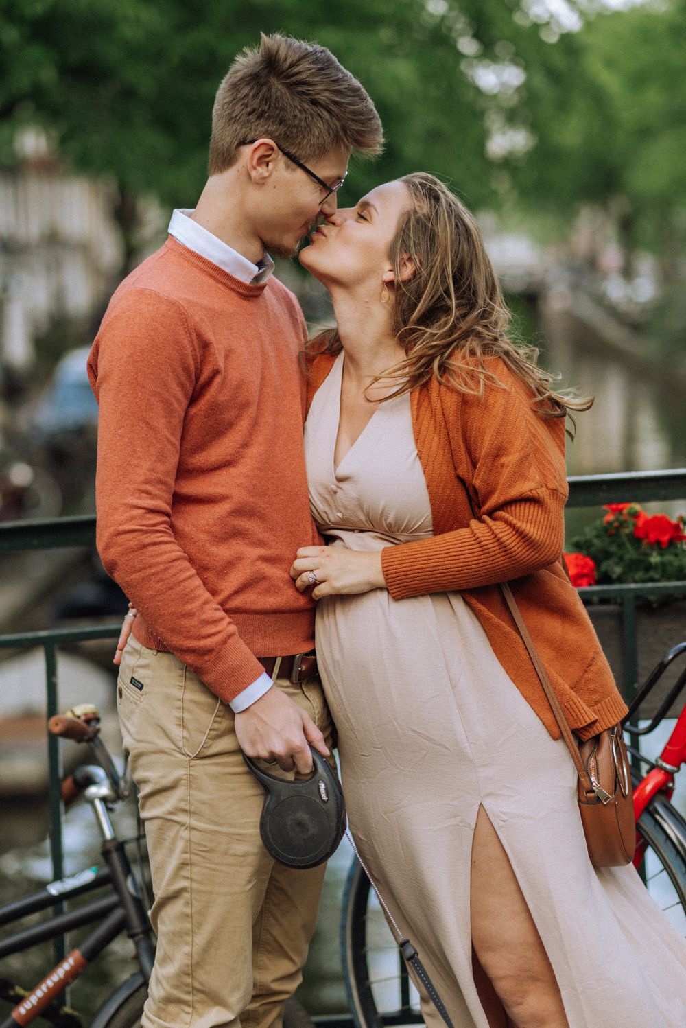 Romantic couple embracing outdoors with orange sweater and white dress.