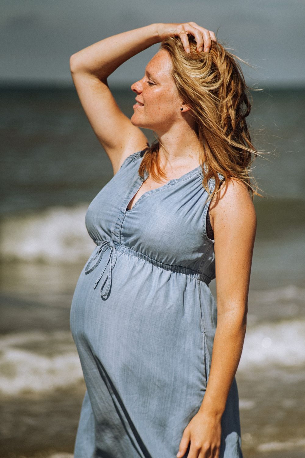 Woman in flowing blue dress poses at beach during golden hour.