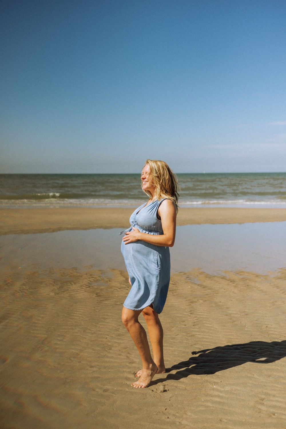 Playful beach photography session with blue dress against ocean backdrop.
