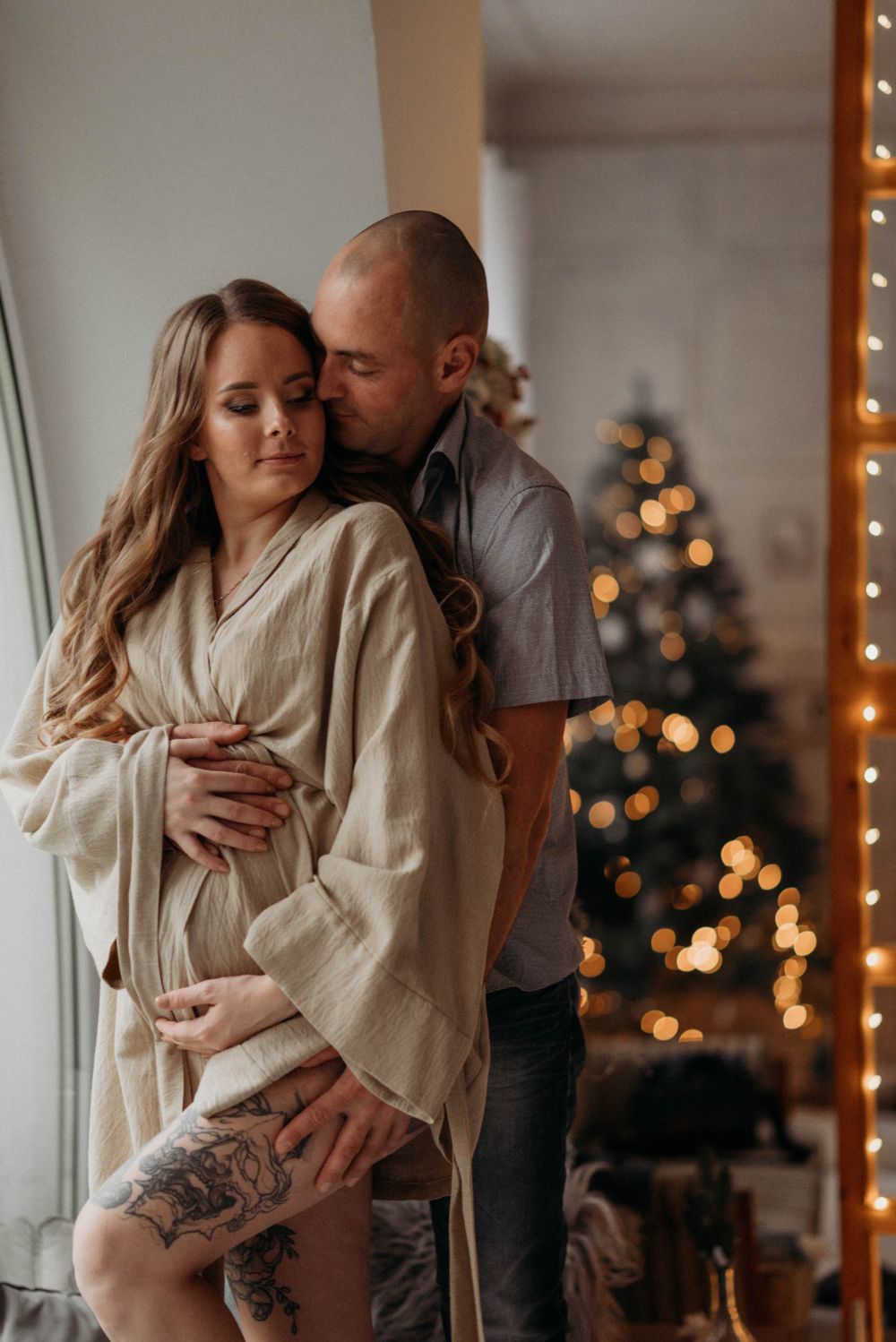 Intimate couple portrait with Christmas tree and string lights in background.
