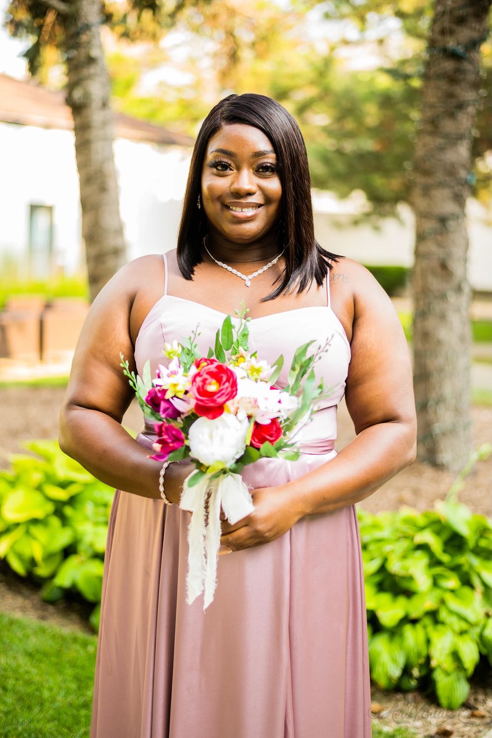 Bridesmaid in dusty rose dress holds colorful bouquet against garden backdrop.