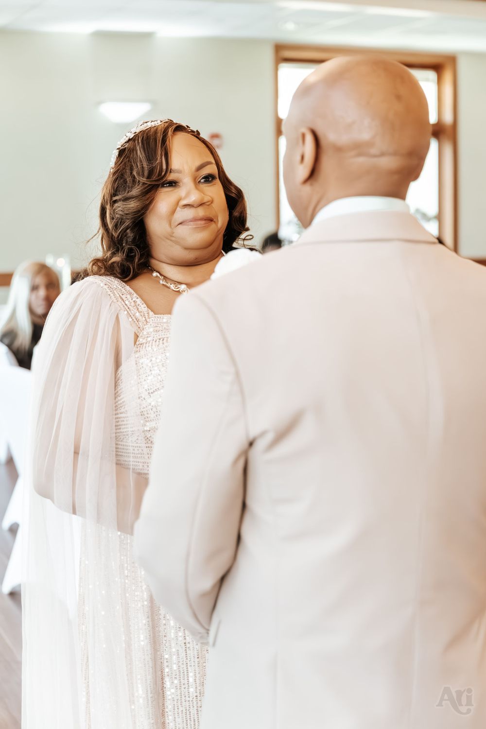 A touching wedding moment captured indoors with the bride wearing a sparkling white gown with flowing sleeves.