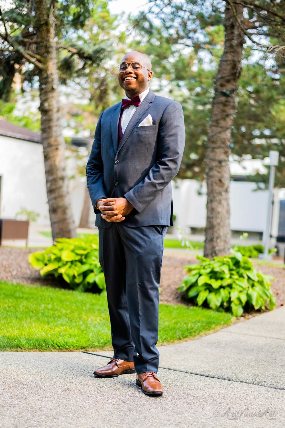 A wedding guest in a sharp navy suit and bowtie poses confidently outdoors.
