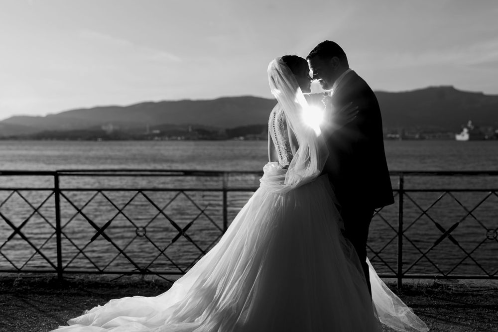 A bride and groom share a romantic silhouette against a waterfront sunset with mountain views.