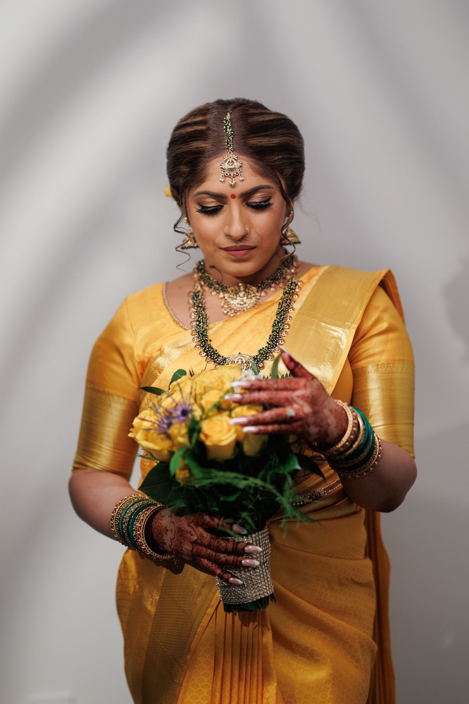 South Asian bride in yellow silk sari holding bouquet during traditional ceremony.