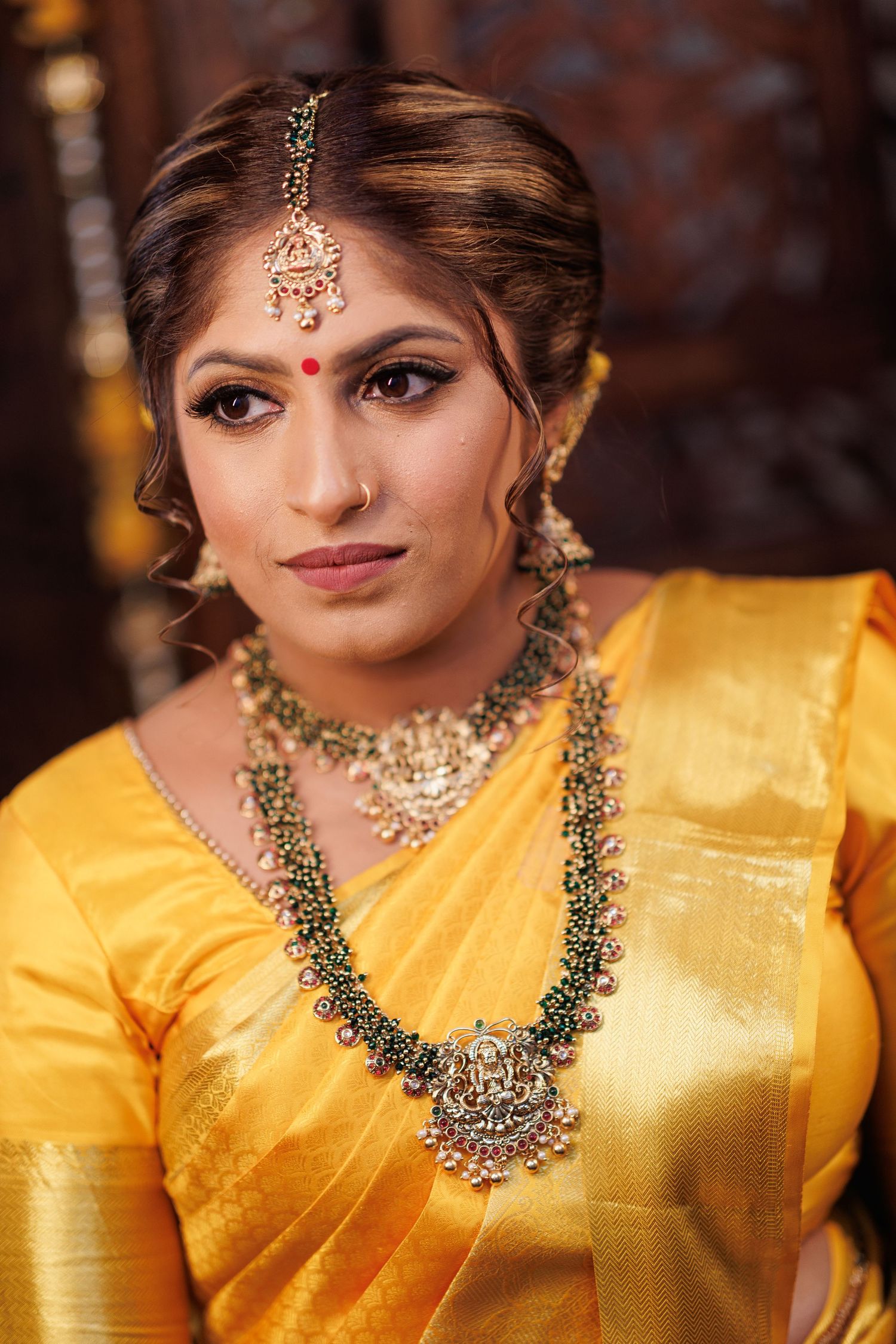Traditional South Asian bridal portrait featuring ornate jewelry and yellow silk attire.