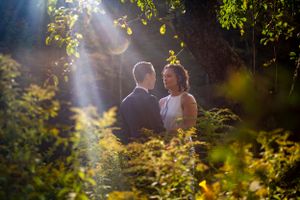 Couple sharing romantic moment surrounded by lush green foliage in sunlit forest.