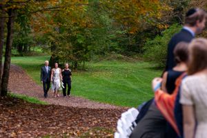 Wedding processional along leaf-covered path through colorful autumn forest setting.