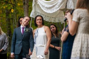 Brides exchanging vows under decorative arch at outdoor woodland wedding.