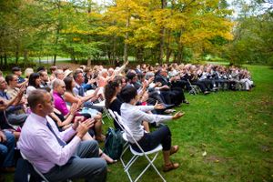 Wedding guests applauding and celebrating during outdoor autumn ceremony on green lawn.