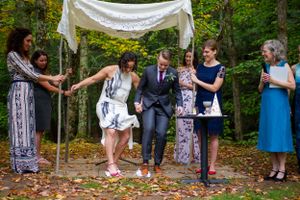 Brides stomp on glass during outdoor Jewish wedding ceremony under chuppah in autumn forest.