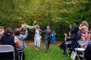 Newlyweds celebrate joyfully as guests cheer during outdoor wedding recessional on green lawn.