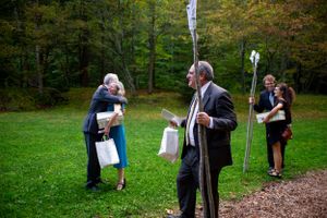 Wedding guests embrace and gather on lawn surrounded by tall trees at outdoor ceremony.