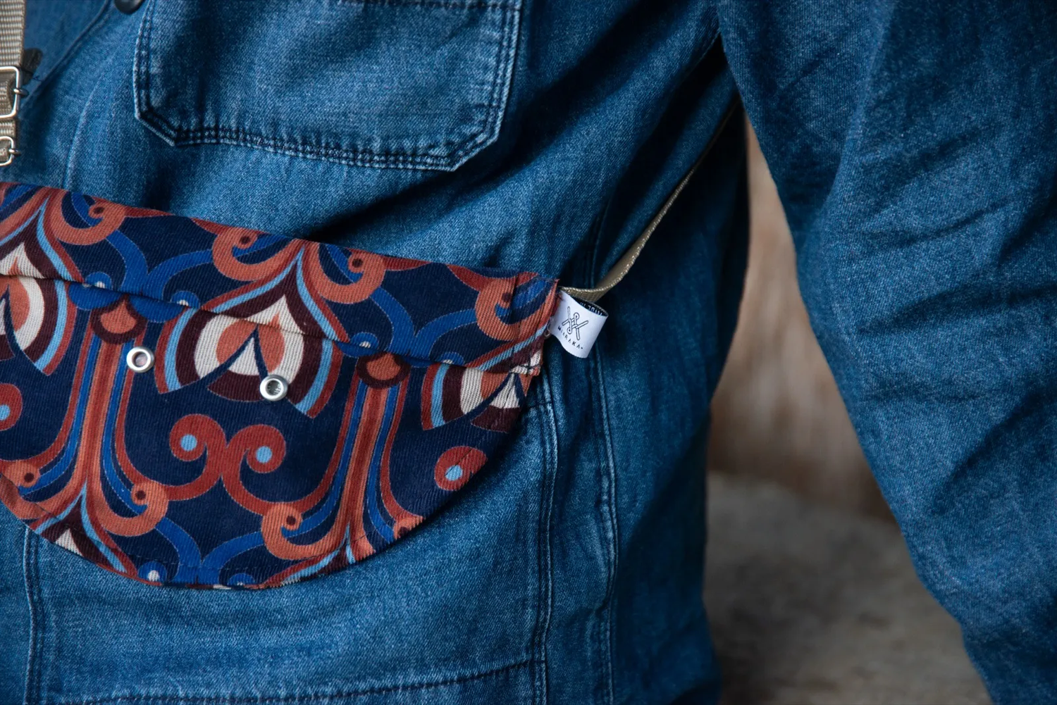 Gros plan sur un dos de veste en jean avec une broderie ornementale rouge et blanche stylisée.