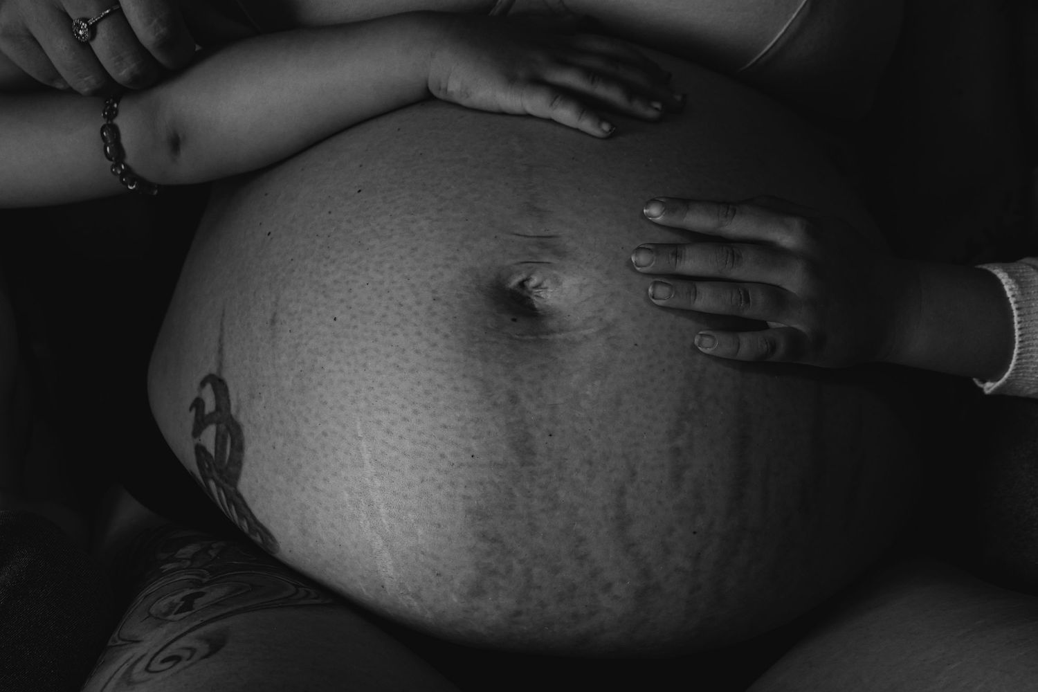 close up on pregnant bump, toddler daughters  with hands resting on mums belly, monochrome, norfolk maternity,