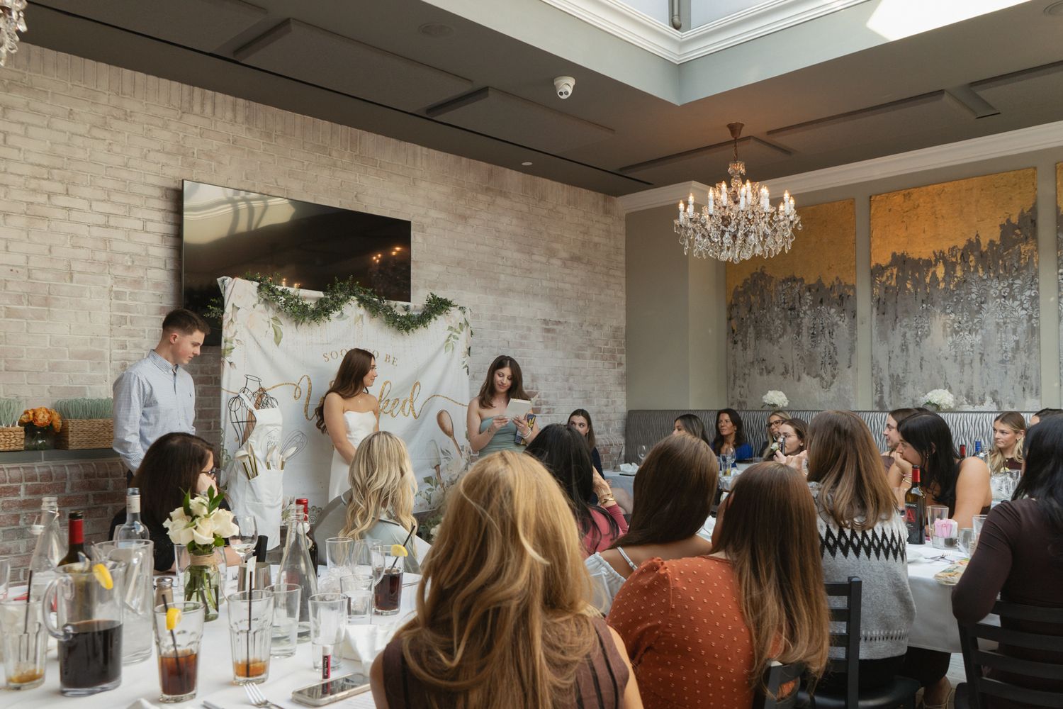 Wedding reception guests mingle and socialize in an elegant venue with exposed brick walls and crystal chandeliers.