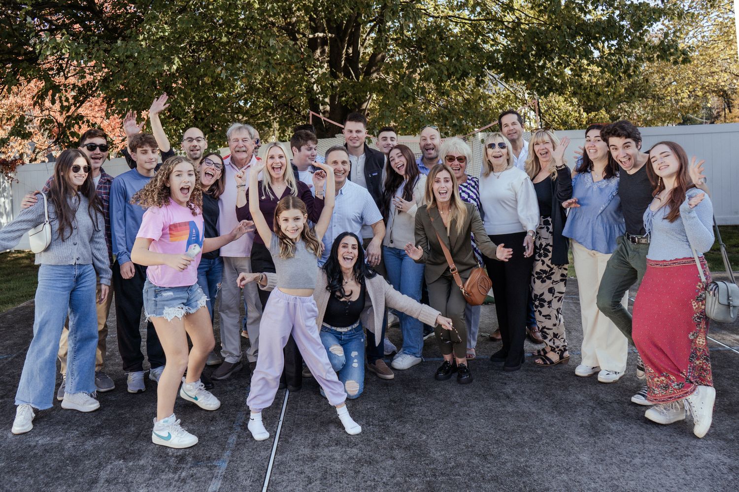 Large group of friends pose together outdoors in casual attire with enthusiastic expressions.