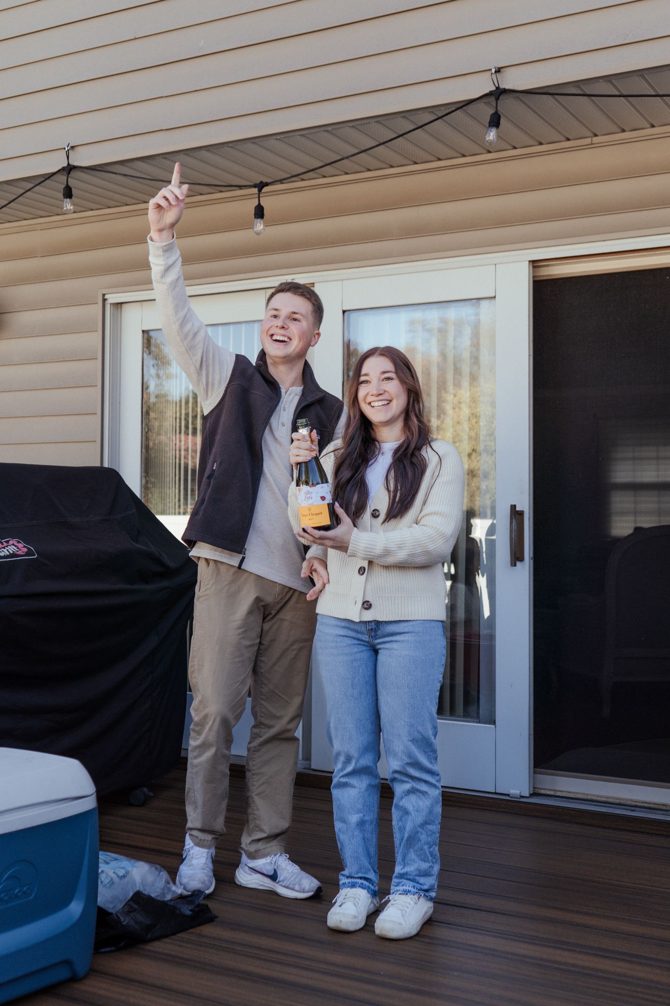 A couple celebrates on their back deck with beverages and excited expressions.