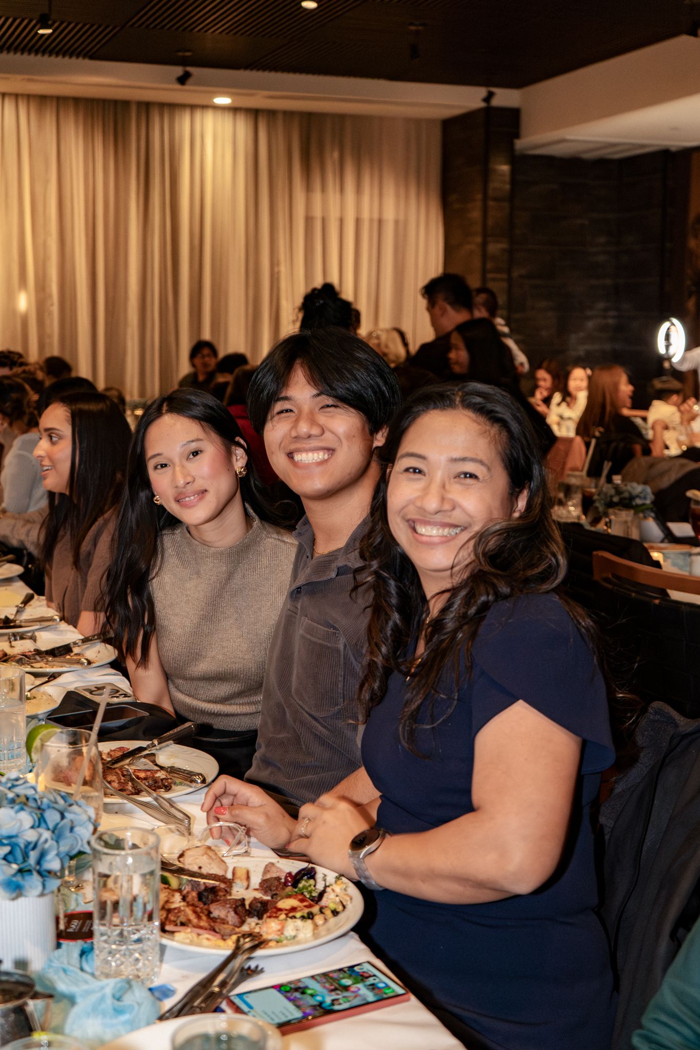 A group of people enjoying a meal together at a dining event with plates of food and drinks on the table.