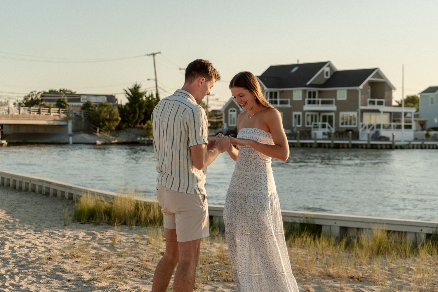 A romantic beachside proposal at sunset with waterfront homes in the background.