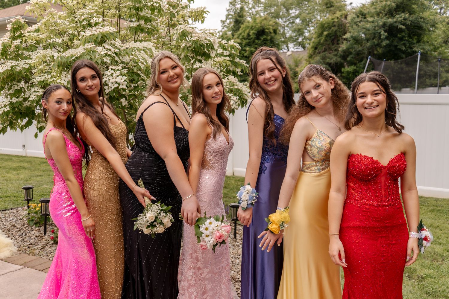 Group photo of people wearing colorful formal dresses at an outdoor celebration.