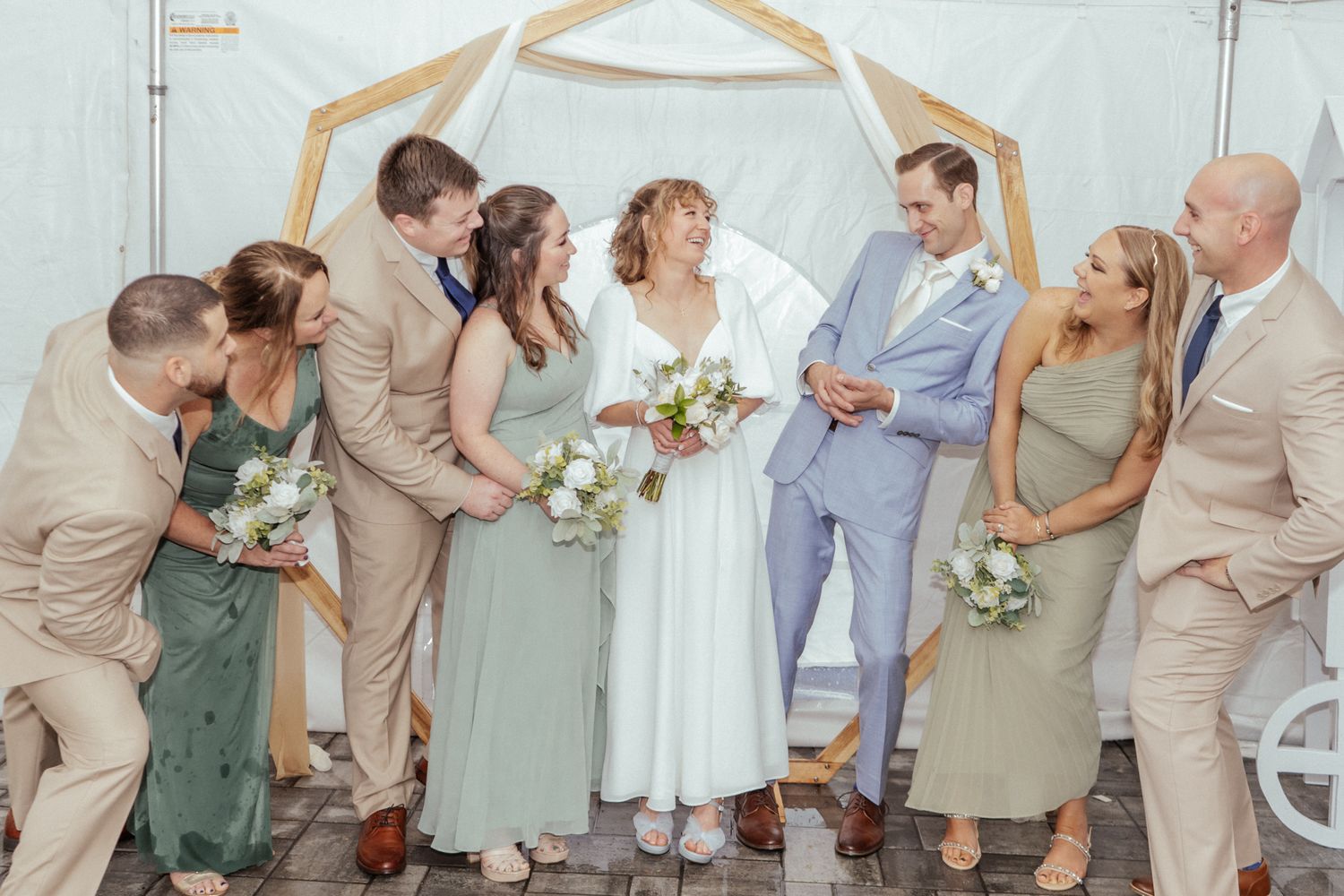 Wedding party members in neutral and sage green attire pose for formal photos.