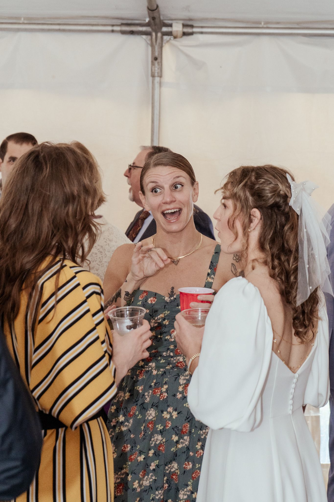 Wedding guests celebrate and laugh together under a white tent at a reception.