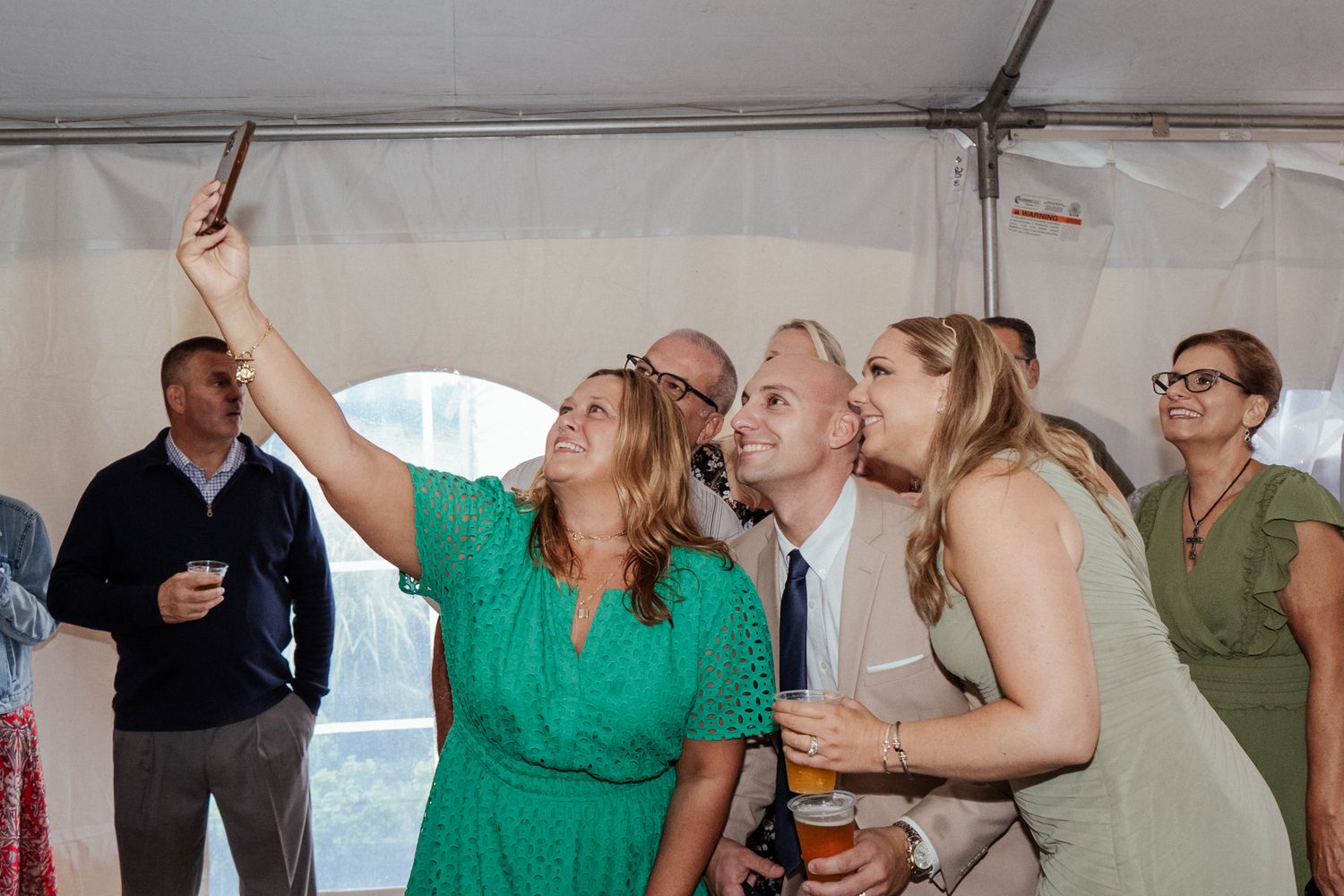 Wedding guests dance and celebrate under a white tent with string lights.
