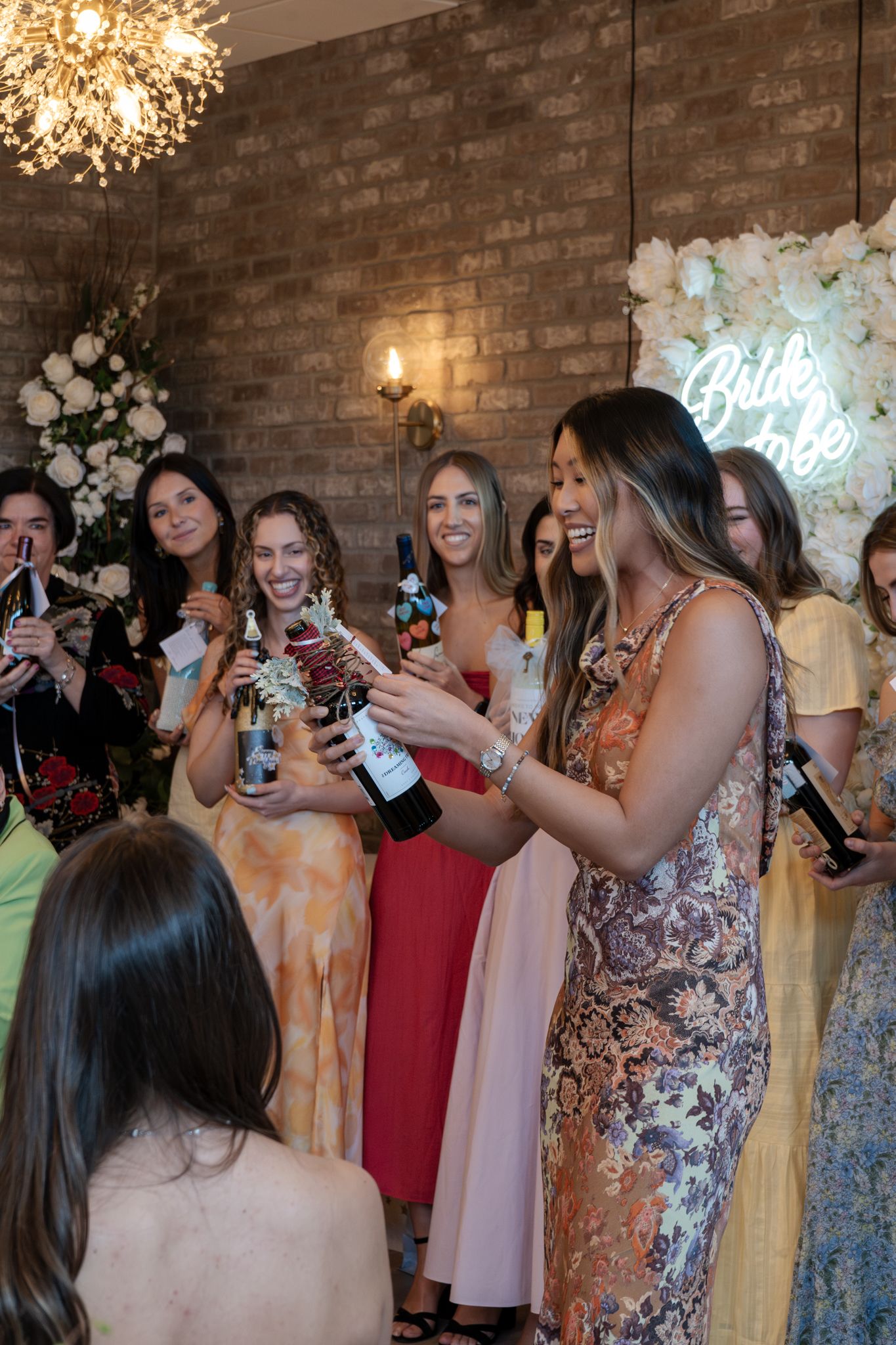 Wedding guests in formal attire taking photos with phones at reception with brick wall backdrop.