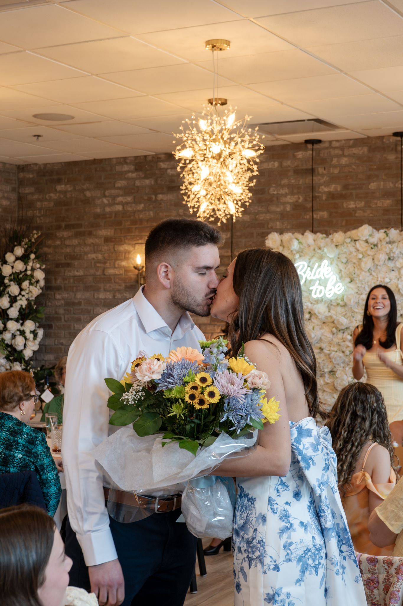 Couple sharing romantic moment at wedding reception with floral wall and chandelier lighting.