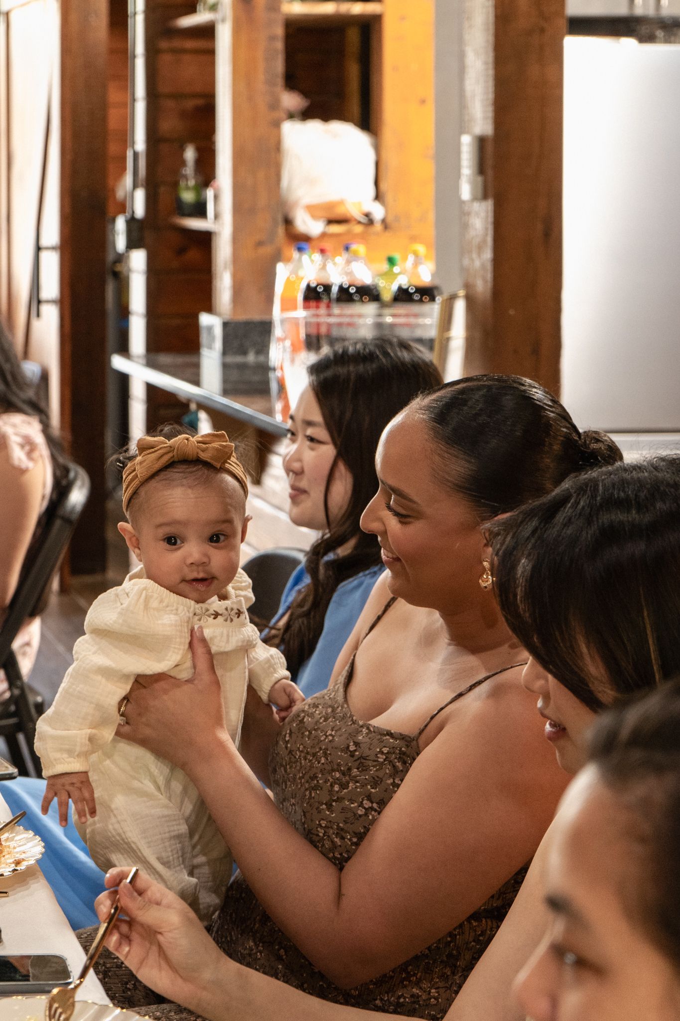 A baby in white clothing is being held during what appears to be a social gathering or celebration.