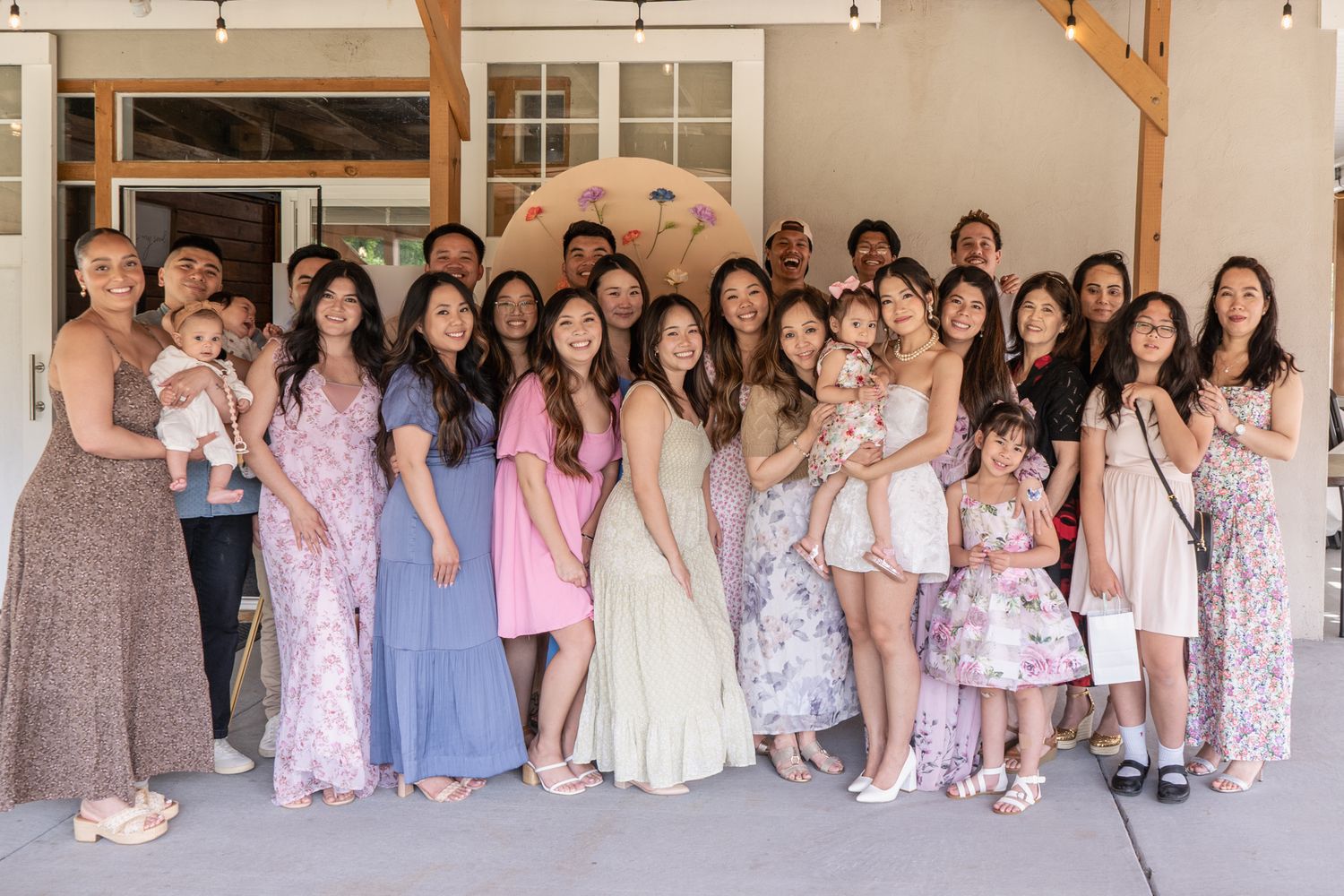 Large group of people in light-colored dresses posing together in front of a rustic building.