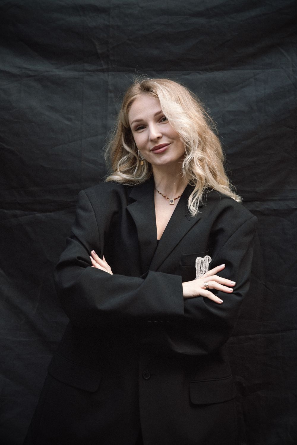 Professional portrait series against a dark backdrop showing a figure in a black blazer with blonde hair striking various poses.