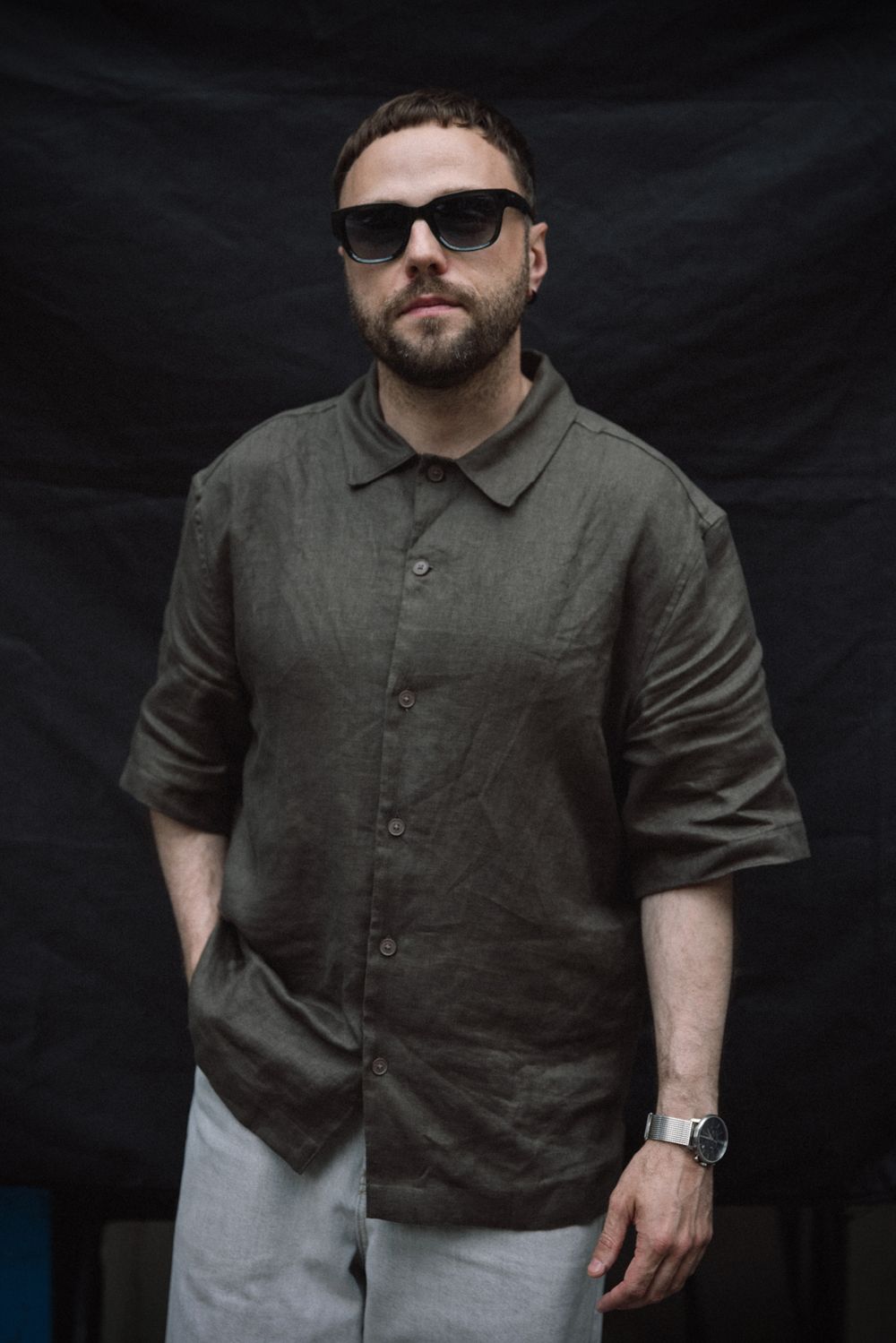 Person wearing a gray collared shirt and light pants poses against a dark background in multiple angles.