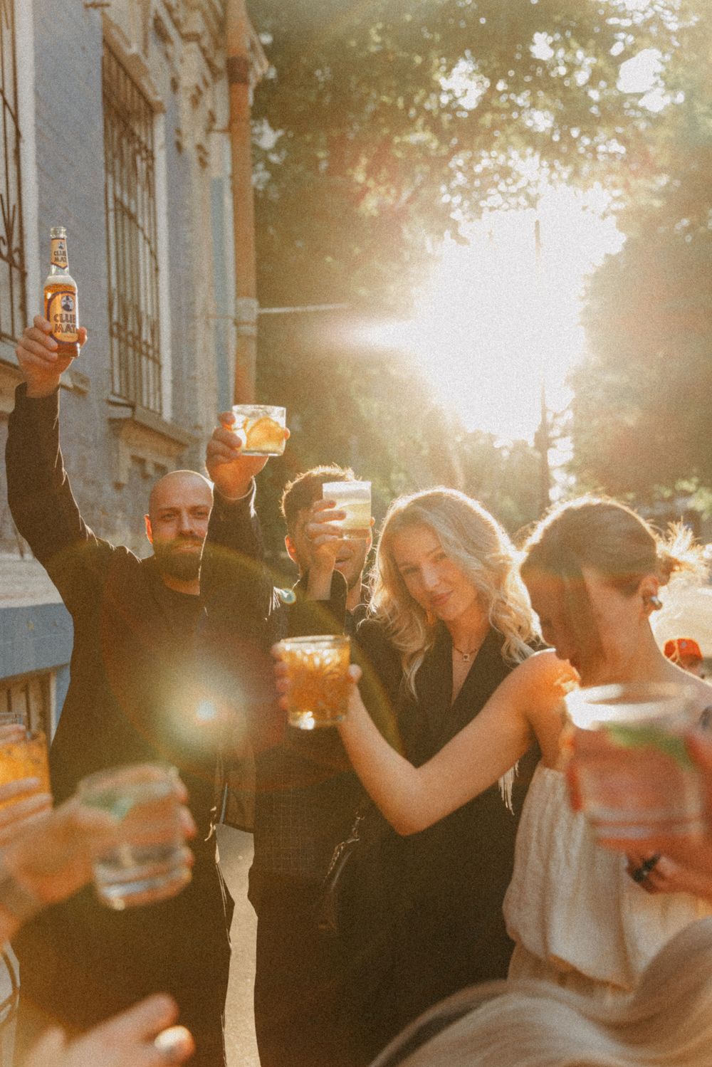 A group of friends toasting with drinks at sunset on a city street, creating a warm and celebratory atmosphere.